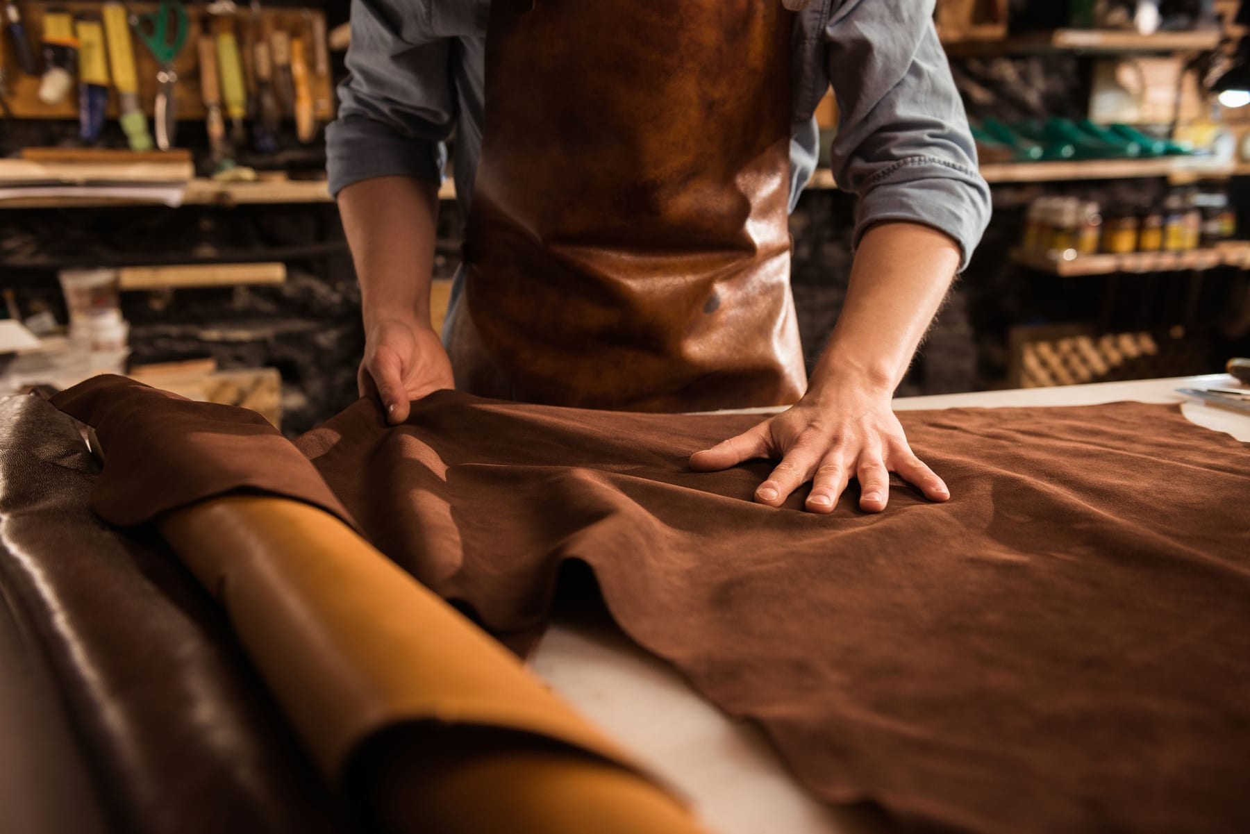 Master craftsman handling leather materials at a workshop bench
